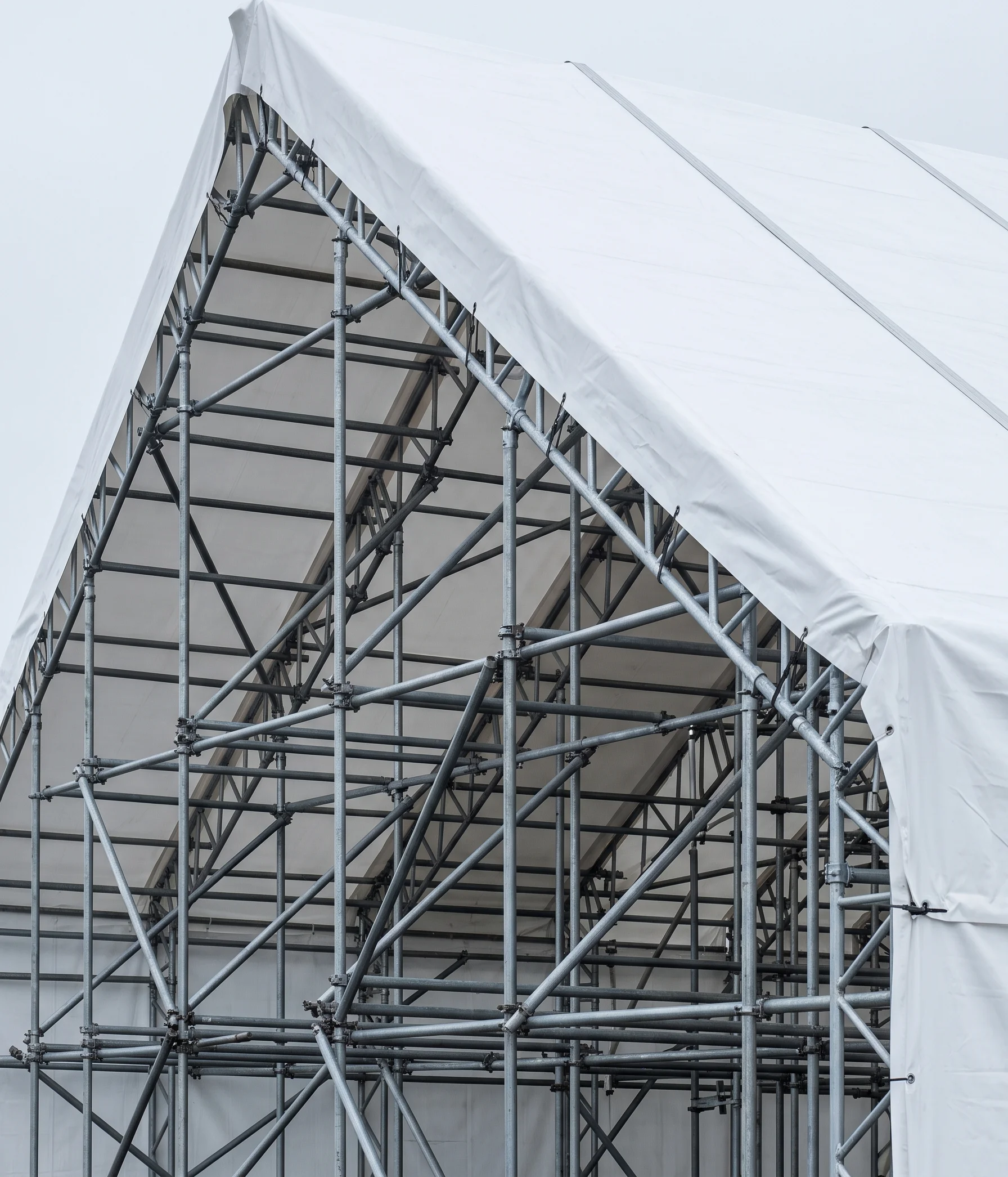 Taut white sheeted temporary roof ridge against a pale grey sky with scaffold tube grid visible beneath